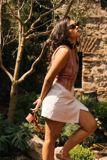Woman in a striped vest and white wrap skirt standing outdoors near a stone building.